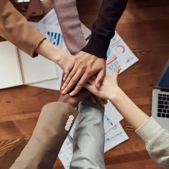 Hände übereinander auf Tisch und Laptop und Papier
